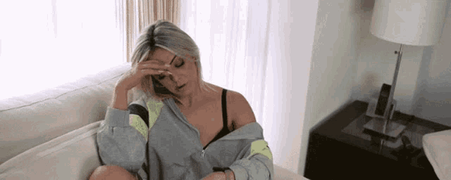 a woman in a bra sits on a couch with her hand on her forehead