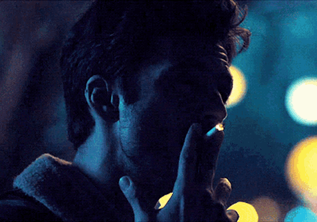 a man smoking a cigarette in the dark with a blurry background
