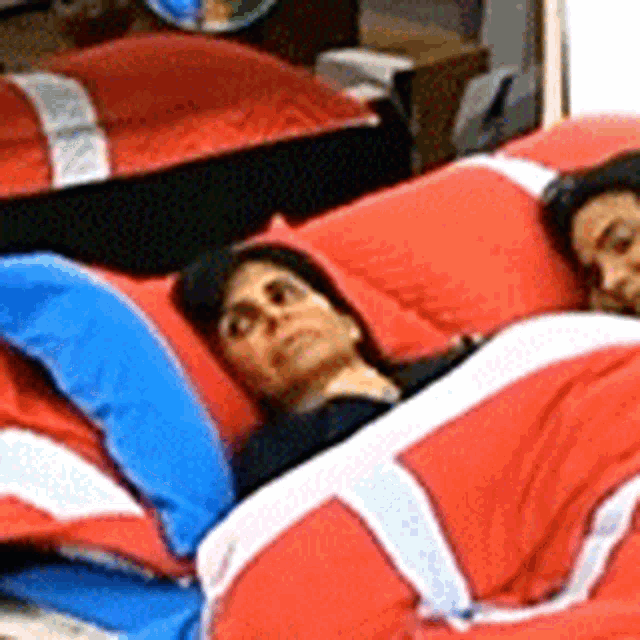 a man and a woman are laying in bed with red and blue sheets