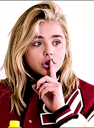 a woman in a red jacket with the number 2 on the sleeve is holding her finger to her mouth .