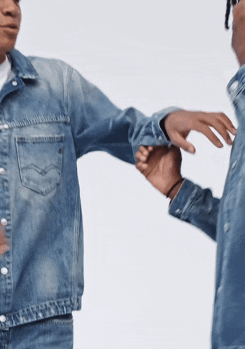 a man in a denim jacket holds the hand of another man in a denim shirt