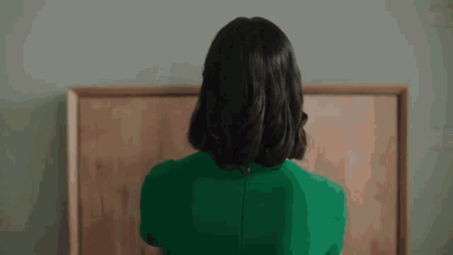 a woman in a green dress stands in front of a wooden bulletin board