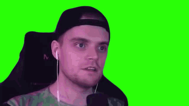 a man wearing headphones and a hat is smiling on a green screen .