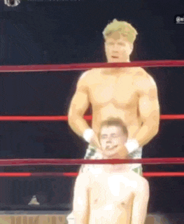 a man is sitting on another man 's back in a boxing ring .