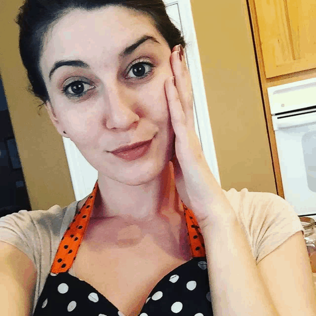 a woman wearing a polka dot apron is touching her face with her hand