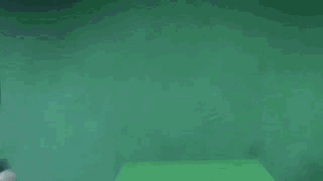 a man in a blue hoodie is jumping in the air on a green background .