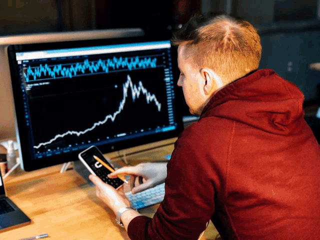 a man in a red hoodie is looking at a graph on a computer
