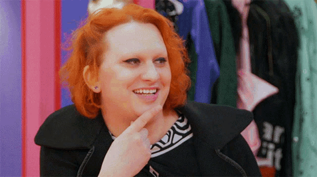 a woman with red hair is smiling with her finger on her chin