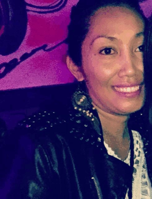 a woman wearing studded earrings and a leather jacket smiles for the camera
