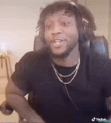 a man wearing headphones and a necklace is sitting in a chair and making a funny face .