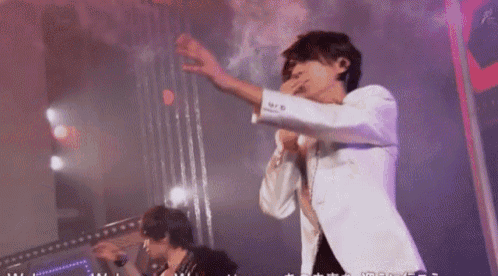 a man in a white suit is singing into a microphone on stage .
