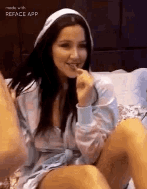 a woman in a hoodie is sitting on a bed with her legs crossed .