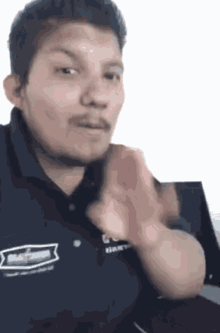 a man in a blue shirt is making a funny face and waving his hand .