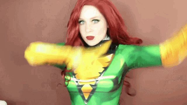 a woman with red hair is wearing a green and yellow costume with her arms outstretched .