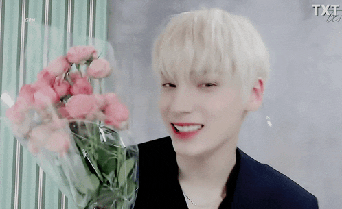 a young man is holding a bouquet of pink roses and the word txt is on the bottom right