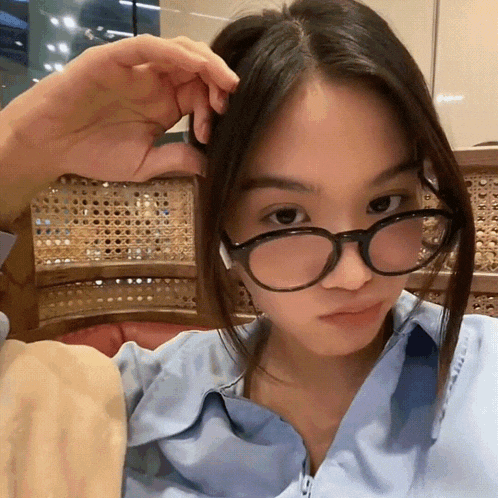 a young woman wearing glasses and a blue shirt looks at the camera