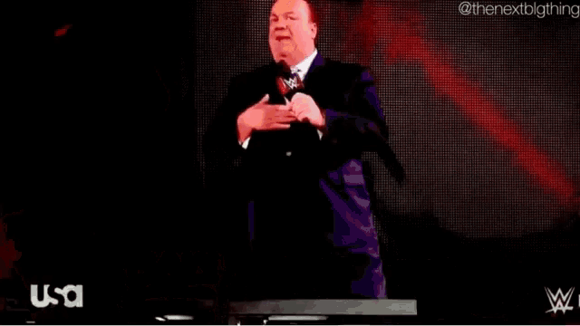 a man in a suit and tie is standing in front of a sign that says paul heyman on it