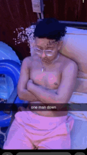 a shirtless man is laying on a bed with his arms crossed and a snapchat caption that says one man down