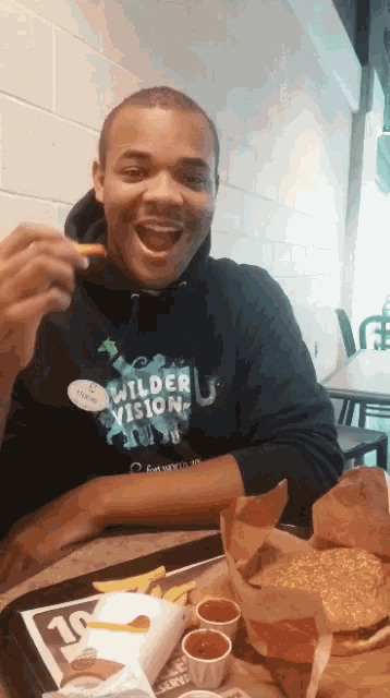 a man wearing a wilder vision sweatshirt is eating a chicken nugget