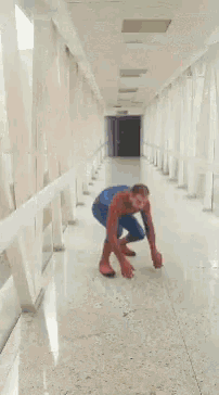 a man in a spiderman costume is crawling on the floor in a hallway .
