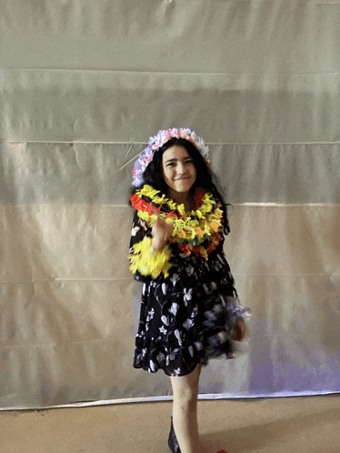 a little girl wearing a black dress and a flower lei around her neck