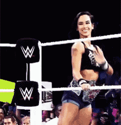 a woman is standing in a wrestling ring with a w on the ropes .