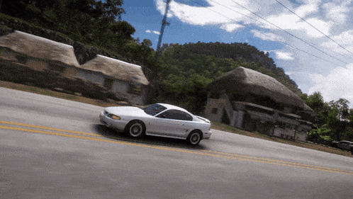 a white car is driving down a road in front of a thatched house