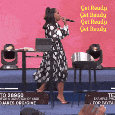 a woman in a polka dot dress singing into a microphone with the words " get ready get ready get ready " behind her