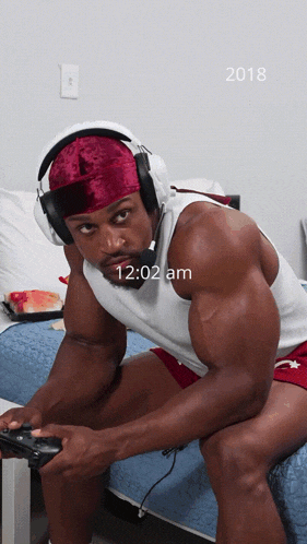 a man wearing headphones sits on a bed at 12:02 am in 2018