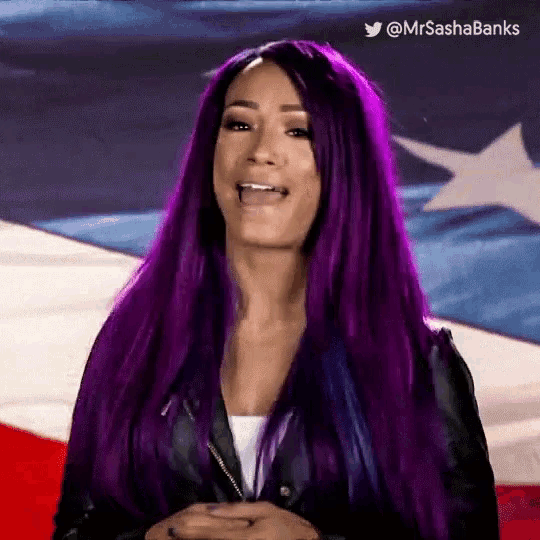 a woman with purple hair is standing in front of an american flag and has the twitter username @mrsashabanks