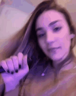 a close up of a woman 's face with purple nails holding her hair .