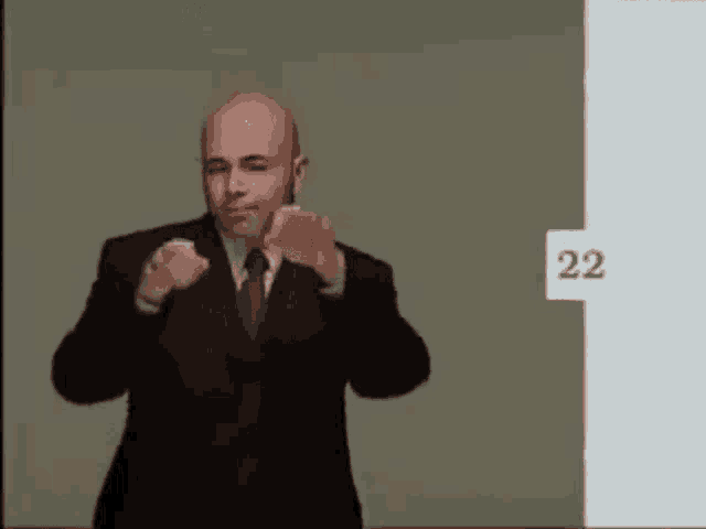 a bald man in a suit and tie is standing in front of a wall with the number 22 on it