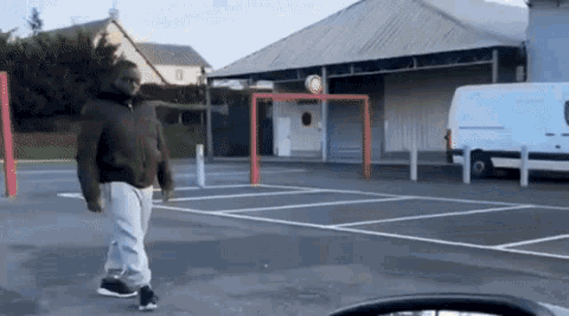 a man is walking in a parking lot with a white van parked in the background .