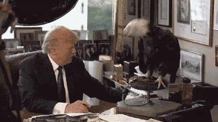 a man in a suit and tie is sitting at a desk with a stuffed eagle on it