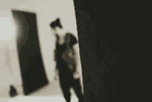 a blurry picture of a person standing in a room with a black wall .