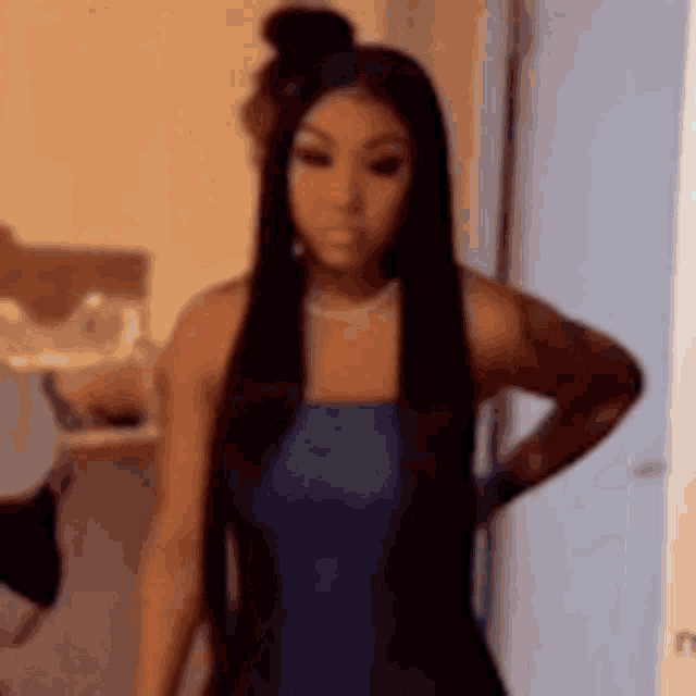 a woman with long black hair is wearing a blue dress and standing in a room .