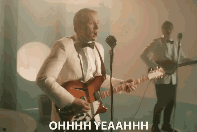 a man in a tuxedo playing a guitar and singing into a microphone with the words ohhhh yeahhh below him