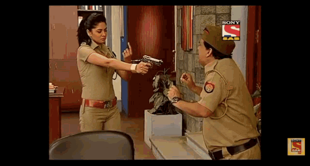 a woman in a police uniform is pointing a gun at a man in a sony sab show .