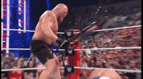 a man is holding a sword in a wrestling ring while a crowd watches .