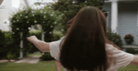 a woman in a white shirt is standing in front of a house with her arms outstretched
