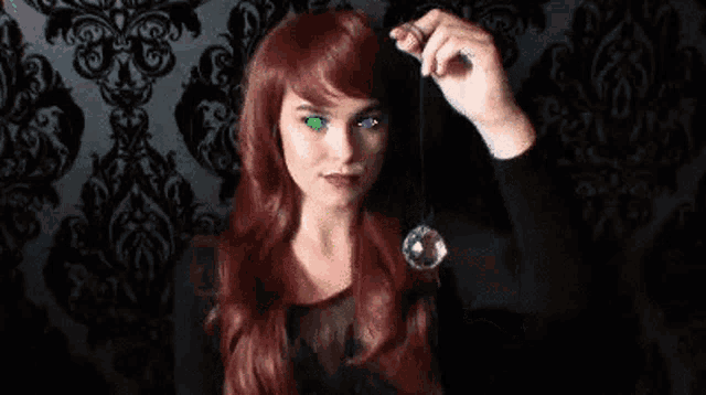a woman with red hair and green eyes is holding a necklace in her hand .