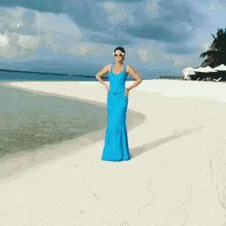 a woman in a blue dress is standing on a sandy beach