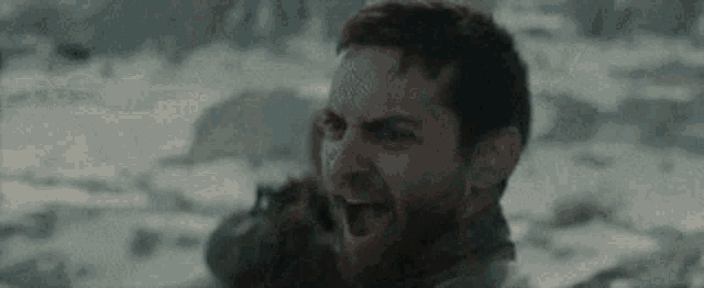 a man with a beard is screaming into a cell phone while standing in the snow .
