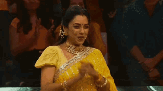 a woman in a yellow sari is clapping her hands in front of a crowd