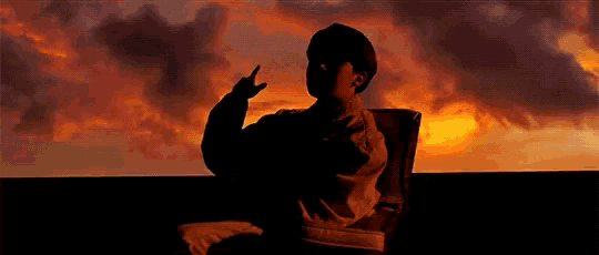 a silhouette of a person standing in front of a sunset with their hands in the air .