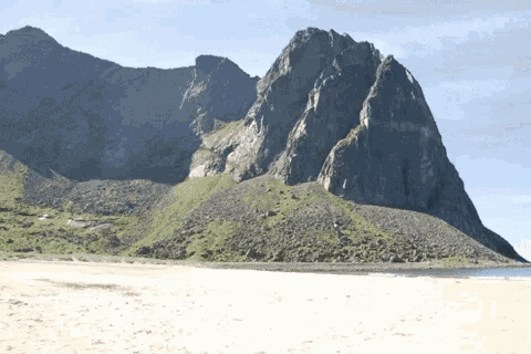 a large rocky mountain with a white sandy beach in the foreground