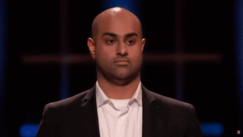 a bald man in a suit and white shirt looks at the camera with a serious look on his face