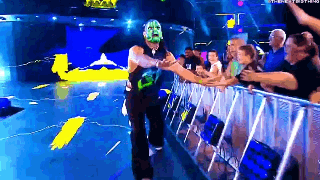 a wrestler in a green mask is shaking hands with a crowd .