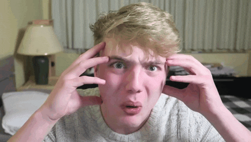 a young man with blonde hair is making a funny face with his hands on his head