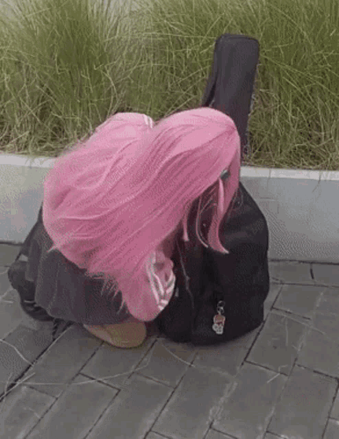 a girl with pink hair is kneeling down next to a black guitar case